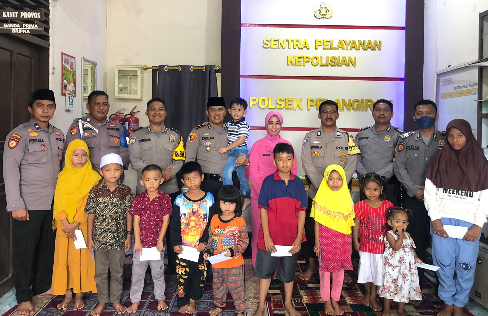 Kapolsek Pelangiran Ipda Delni Atma Saputra, SH, MH didampingi Ketua Bhayangkari Ranting Pelangiran Ria Delni dan personil Polsek Pelangiran bersama anak yatim yang mendapatkan santunan.